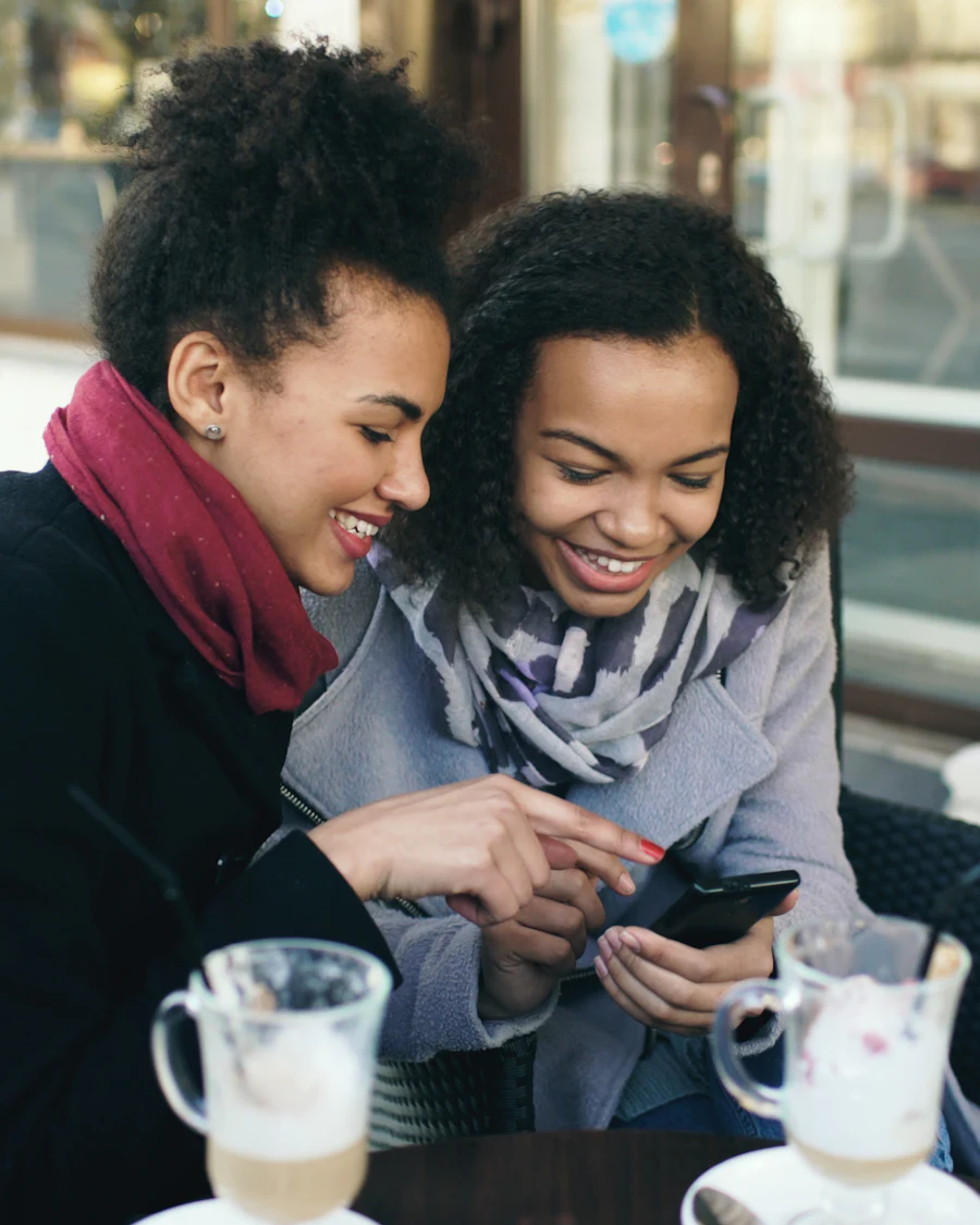 Duas amigas sorrindo enquanto olham um convite no celular
